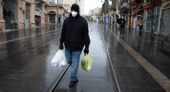 A man walking with groceries in an empty street in Jerusalem. Photo: Amit Shabi