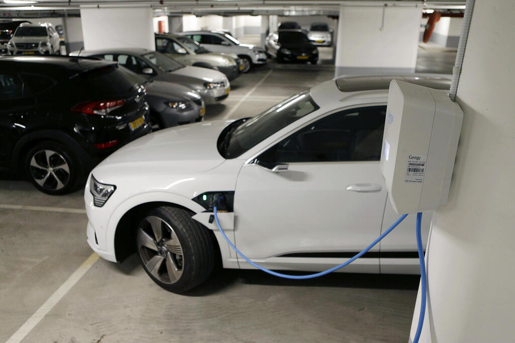 רכב אאודי לבן חשמלי ב טעינה ב חניון בניין משותף מכונית חשמלית 
